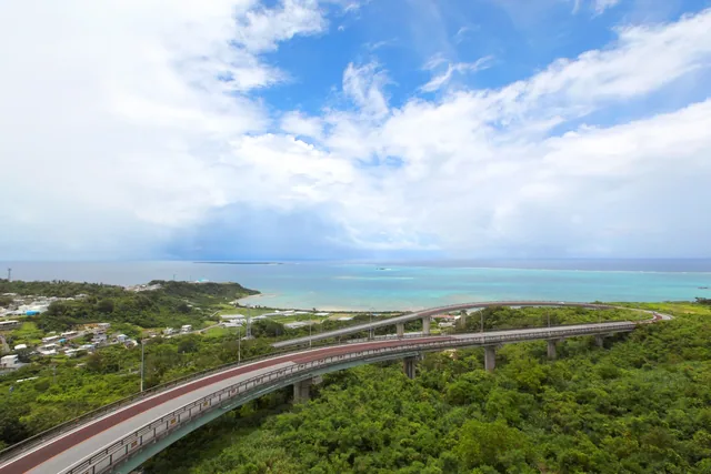 南城市の緑の丘から青い海へ向かってカーブを描くニライ橋・カナイ橋